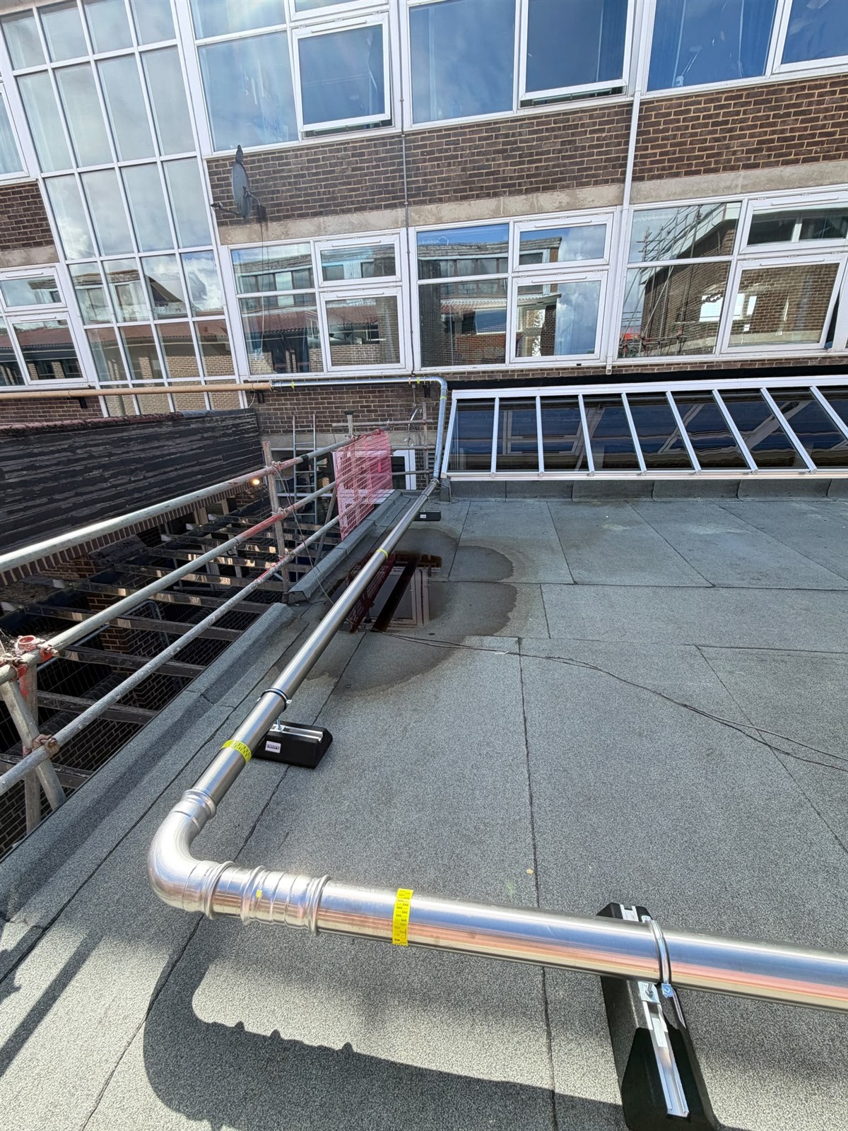 Supported stainless steel gas main turning around the school roof edge
